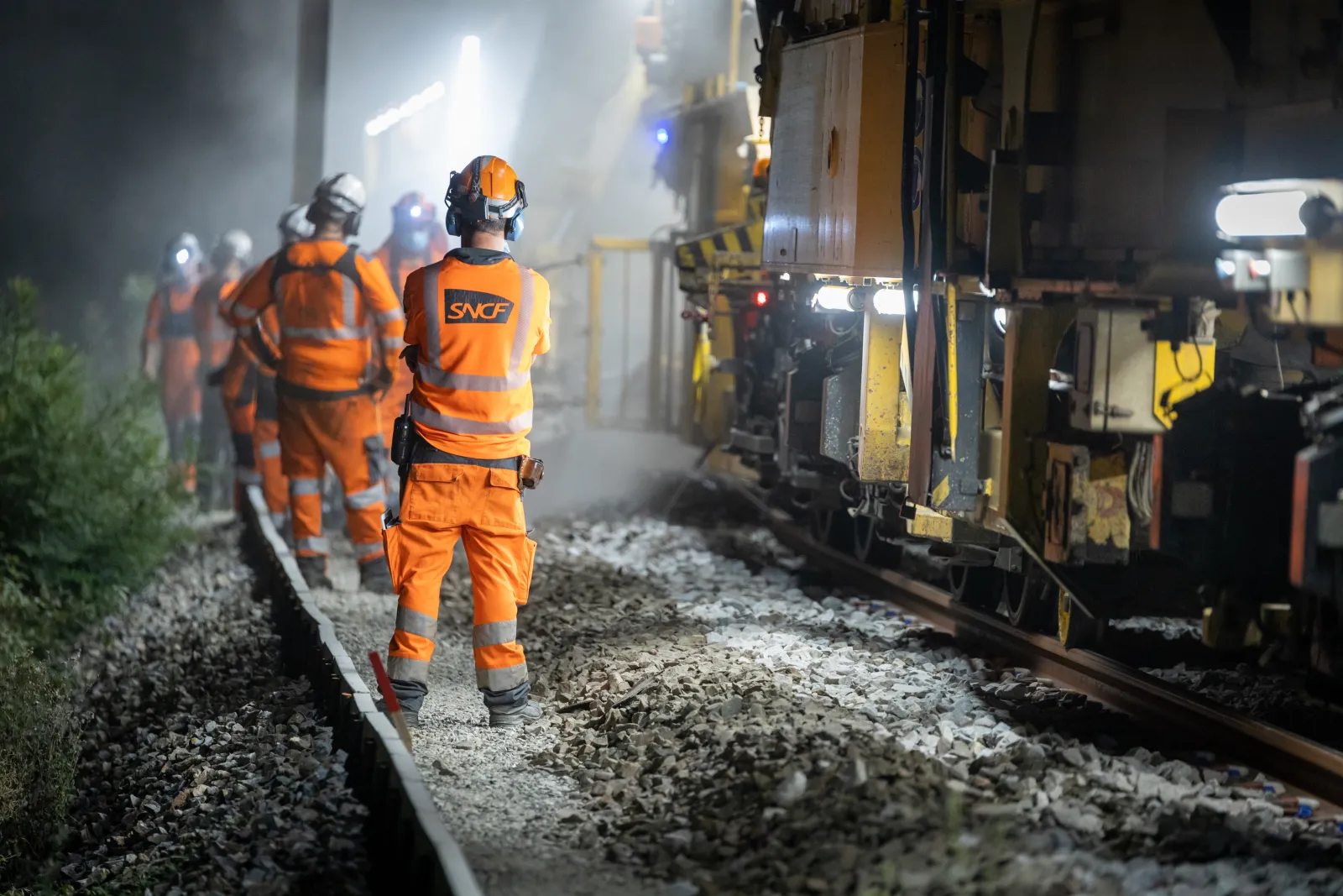 Agents SNCF de dos face à un train de travaux, sur un chantier de nuit